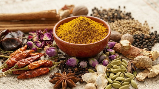 Bowl of Ras el Hanout surrounded by assorted whole spices, dried rose buds, cinnamon, cardamom, and peppers.